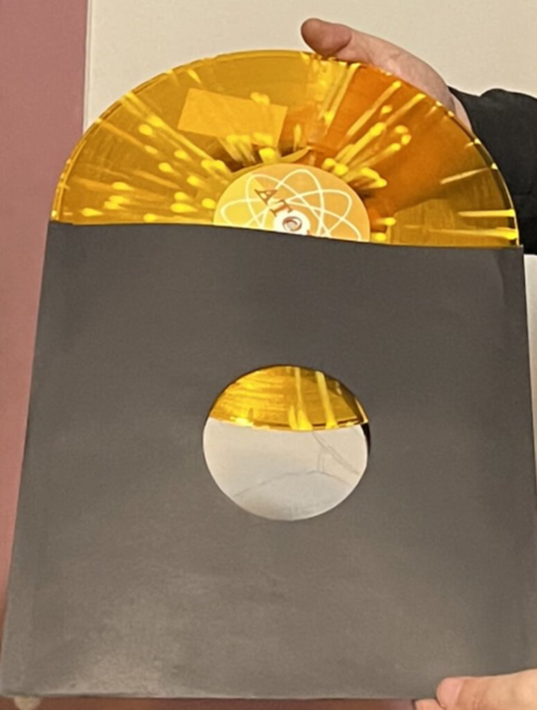 An translucent Orange w/ yellow wax drip colored LP album by Sun Atoms entitled Let there be light, pulled halfway out of the sleeve.