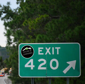 A freeway exit sign says exit 420 with a House of Cannabis sticker applied